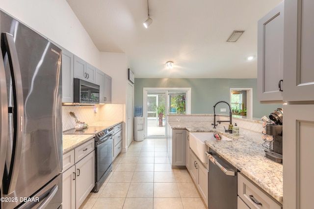 kitchen featuring light tile patterned flooring, appliances with stainless steel finishes, tasteful backsplash, sink, and light stone counters