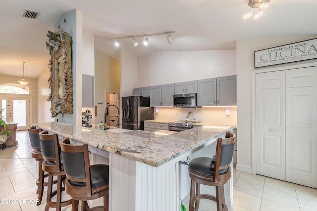 kitchen with light stone countertops, stainless steel appliances, kitchen peninsula, and a kitchen bar