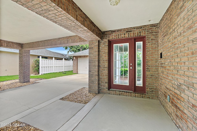 doorway to property featuring driveway, fence, and brick siding
