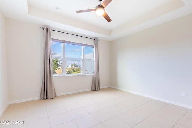 empty room featuring a raised ceiling, ceiling fan, and light tile patterned floors