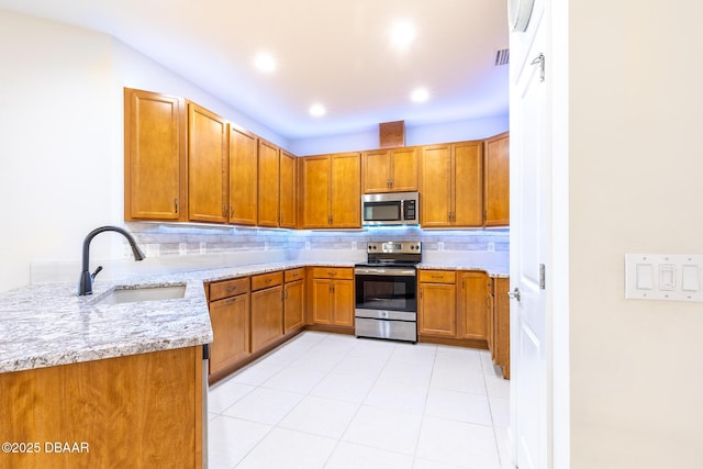 kitchen featuring light stone countertops, kitchen peninsula, tasteful backsplash, stainless steel appliances, and sink