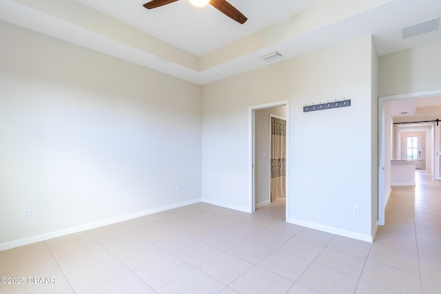 tiled empty room featuring a tray ceiling and ceiling fan