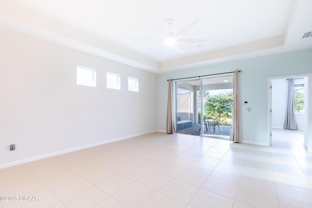 tiled empty room with ceiling fan and a raised ceiling