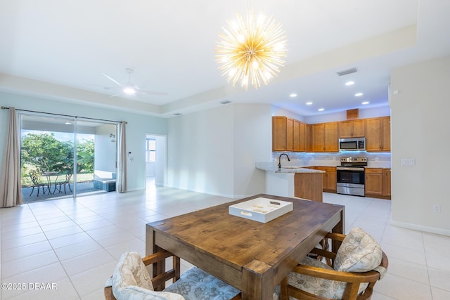 dining room with a tray ceiling, sink, light tile patterned floors, and ceiling fan with notable chandelier