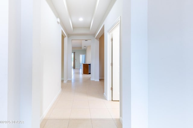 hallway featuring light tile patterned floors and a tray ceiling