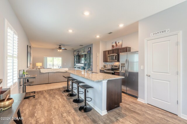 kitchen with sink, appliances with stainless steel finishes, a kitchen bar, dark brown cabinets, and a kitchen island with sink