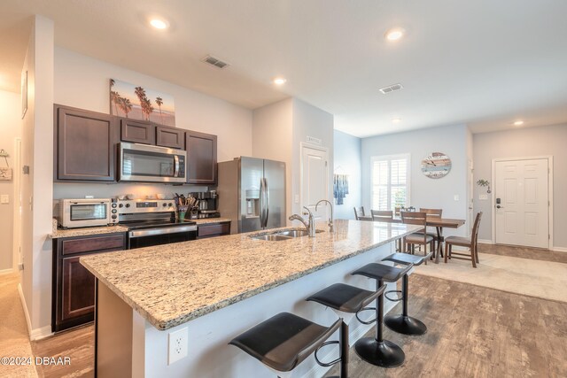 kitchen with a kitchen bar, a center island with sink, sink, dark brown cabinets, and appliances with stainless steel finishes