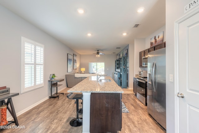 kitchen featuring stainless steel appliances, a kitchen bar, light stone countertops, an island with sink, and light hardwood / wood-style floors