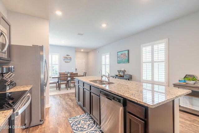 kitchen with stainless steel appliances, plenty of natural light, an island with sink, and light wood-type flooring