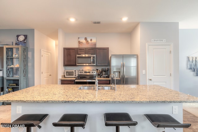 kitchen with stainless steel appliances, dark brown cabinetry, sink, a breakfast bar area, and a kitchen island with sink