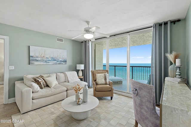 living room featuring expansive windows, a water view, and ceiling fan