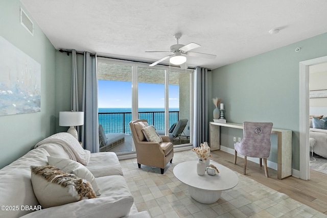 living room featuring ceiling fan, a water view, a textured ceiling, and light wood-type flooring