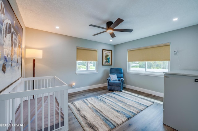 bedroom with hardwood / wood-style floors, a textured ceiling, ceiling fan, and a nursery area