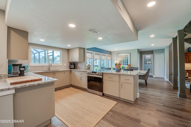 kitchen featuring light stone countertops, stainless steel range with electric cooktop, light hardwood / wood-style floors, sink, and kitchen peninsula