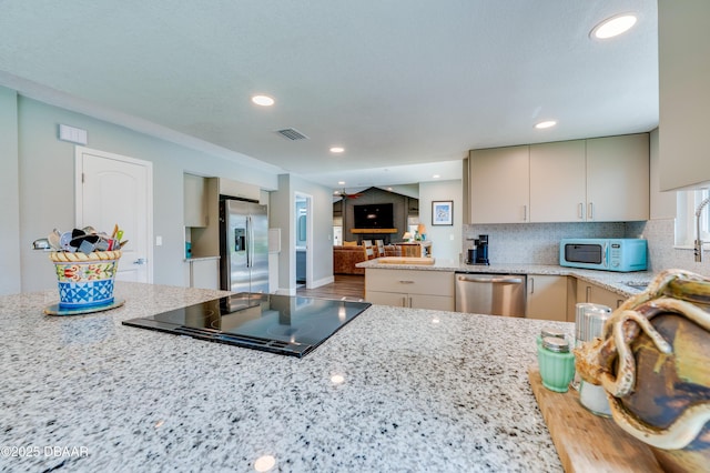 kitchen with light stone counters, decorative backsplash, cream cabinets, and stainless steel appliances