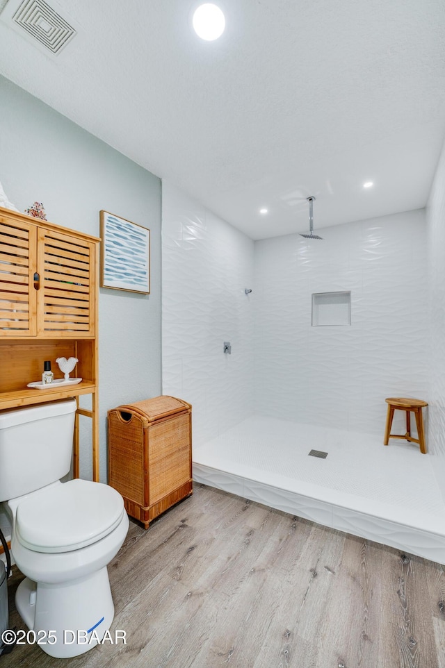 bathroom with toilet, tiled shower, and hardwood / wood-style flooring