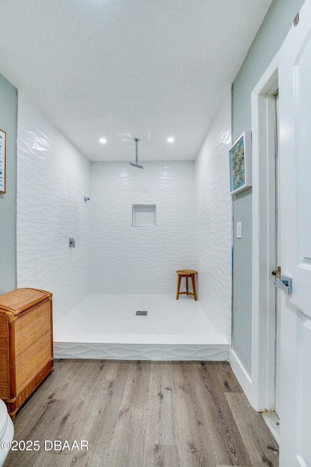 bathroom featuring hardwood / wood-style flooring, tiled shower, and toilet