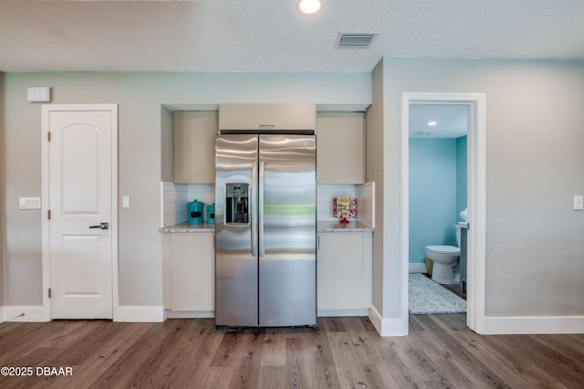 kitchen featuring light stone countertops, hardwood / wood-style floors, a textured ceiling, decorative backsplash, and stainless steel fridge with ice dispenser