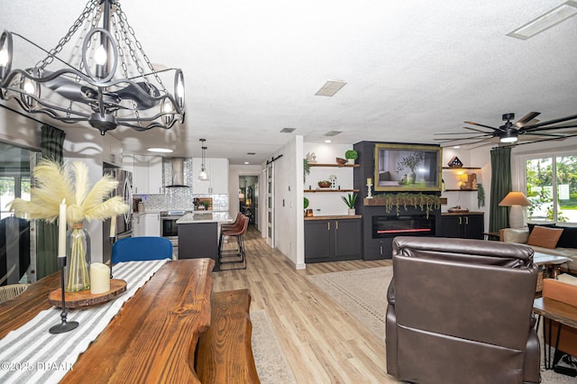 792 N Beach St, Ormond Beach, FL 32174 - dining room with a glass covered fireplace, light wood-style flooring, a chandelier, a ceiling fan, and a textured ceiling