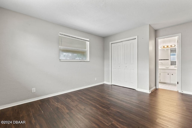 unfurnished bedroom with a textured ceiling, dark hardwood / wood-style floors, ensuite bath, and a closet