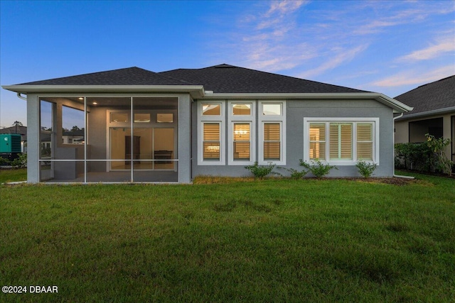 back house at dusk featuring a sunroom and a yard