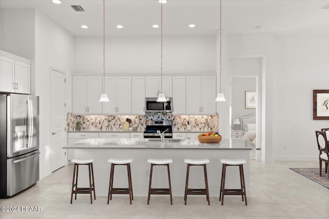 kitchen featuring appliances with stainless steel finishes, hanging light fixtures, an island with sink, and white cabinets