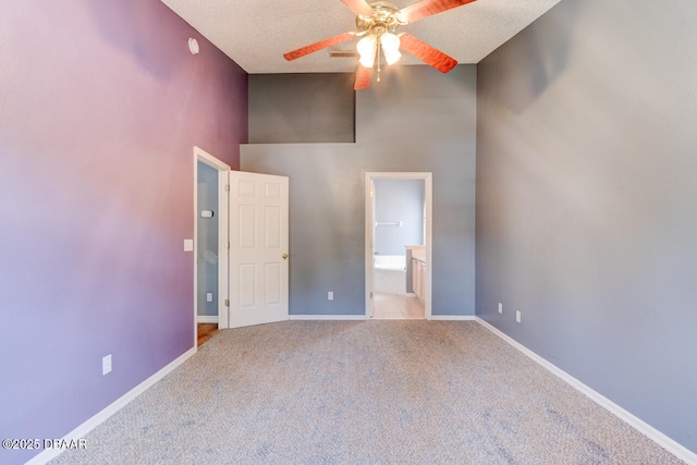 unfurnished room featuring ceiling fan, baseboards, a towering ceiling, a textured ceiling, and carpet floors