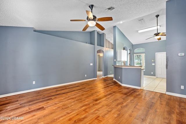 unfurnished living room with a textured ceiling, high vaulted ceiling, sink, light hardwood / wood-style floors, and ceiling fan