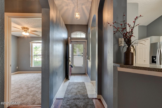 entryway with a textured ceiling, a wealth of natural light, light tile patterned floors, and baseboards