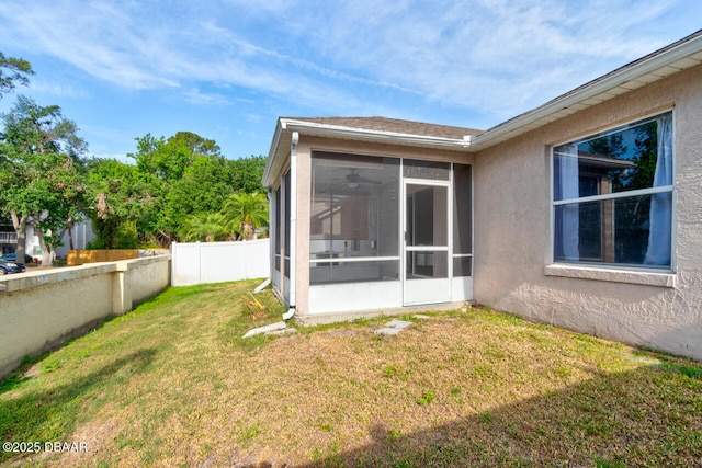 back of property with stucco siding, fence, a yard, and a sunroom