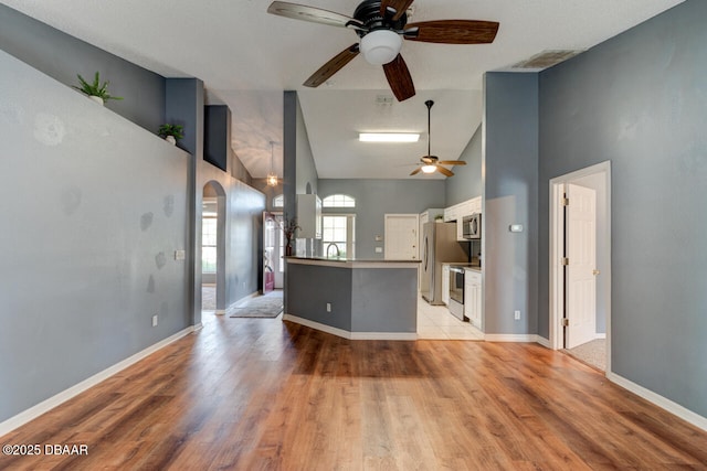 unfurnished living room featuring light wood-style flooring, a ceiling fan, high vaulted ceiling, and baseboards