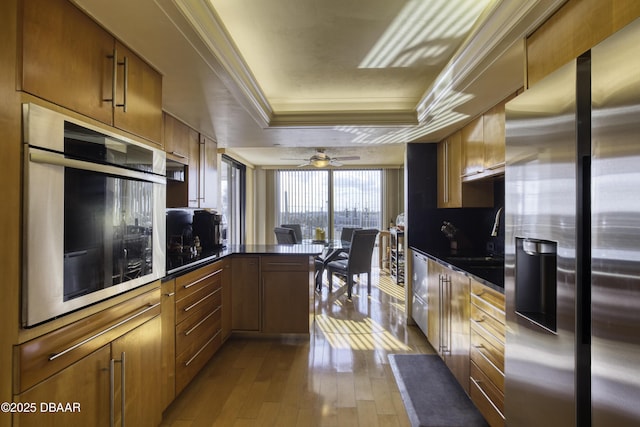 kitchen featuring sink, appliances with stainless steel finishes, a tray ceiling, ornamental molding, and light wood-type flooring