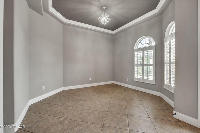 tiled empty room with a chandelier, crown molding, and a tray ceiling