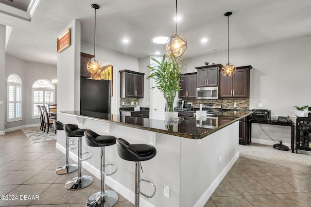 kitchen with stainless steel appliances, tasteful backsplash, decorative light fixtures, and dark stone countertops