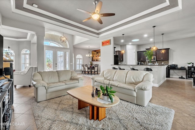 tiled living room with crown molding, ceiling fan with notable chandelier, french doors, and a raised ceiling