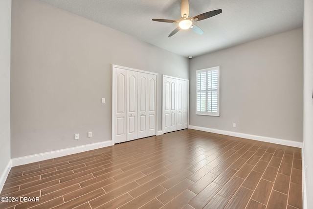 unfurnished bedroom with dark wood-type flooring, a textured ceiling, ceiling fan, and multiple closets