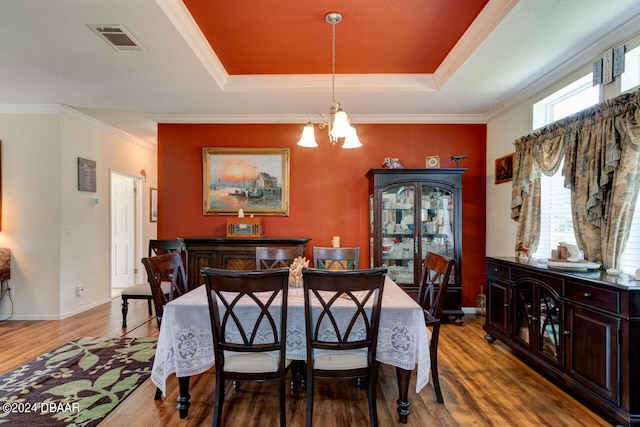 dining room with ornamental molding, a notable chandelier, light hardwood / wood-style flooring, and a tray ceiling