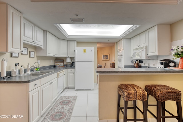 kitchen with white appliances, a kitchen breakfast bar, and white cabinets