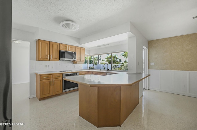 kitchen featuring brown cabinets, appliances with stainless steel finishes, light speckled floor, and light countertops