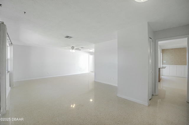 empty room with visible vents, baseboards, speckled floor, and ceiling fan