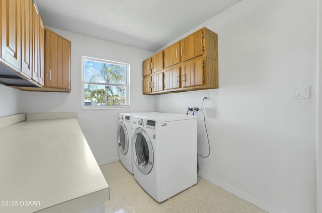 washroom with a textured ceiling, cabinet space, baseboards, and washer and clothes dryer