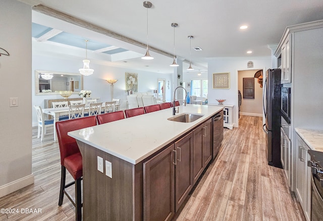 kitchen with a kitchen bar, a center island with sink, sink, pendant lighting, and light hardwood / wood-style flooring