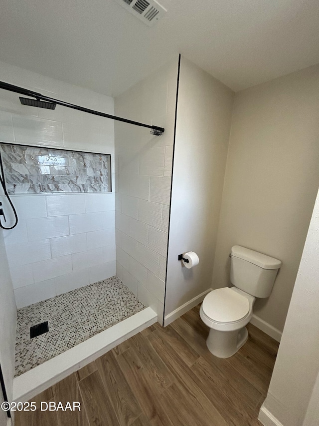 bathroom with tiled shower, toilet, and hardwood / wood-style floors