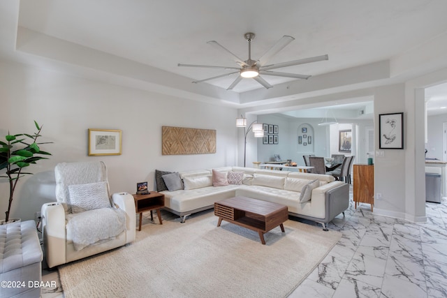 living room featuring a raised ceiling and ceiling fan