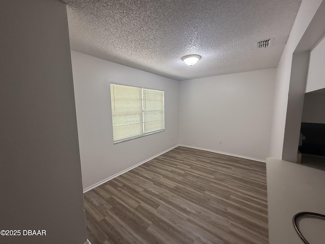 empty room with baseboards, a textured ceiling, dark wood-style floors, and visible vents