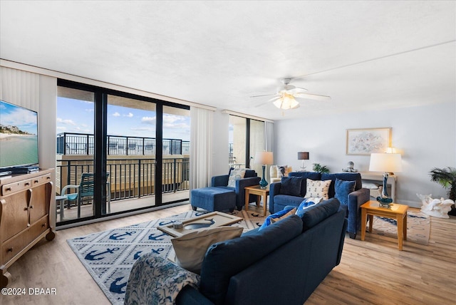 living room featuring ceiling fan, a wall of windows, and light hardwood / wood-style flooring