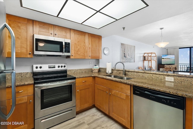 kitchen featuring sink, stainless steel appliances, kitchen peninsula, dark stone countertops, and light wood-type flooring