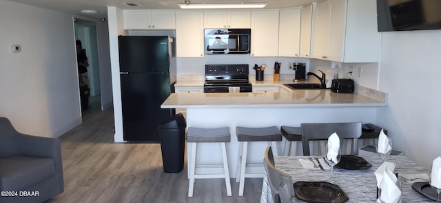 kitchen featuring black appliances, a kitchen breakfast bar, sink, white cabinetry, and kitchen peninsula