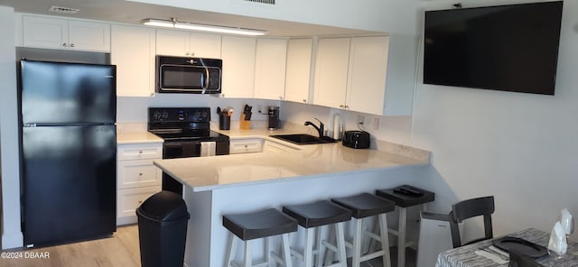 kitchen with kitchen peninsula, white cabinetry, black appliances, and light hardwood / wood-style floors