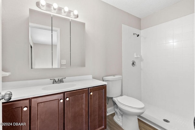 bathroom featuring hardwood / wood-style flooring, a textured ceiling, vanity, tiled shower, and toilet